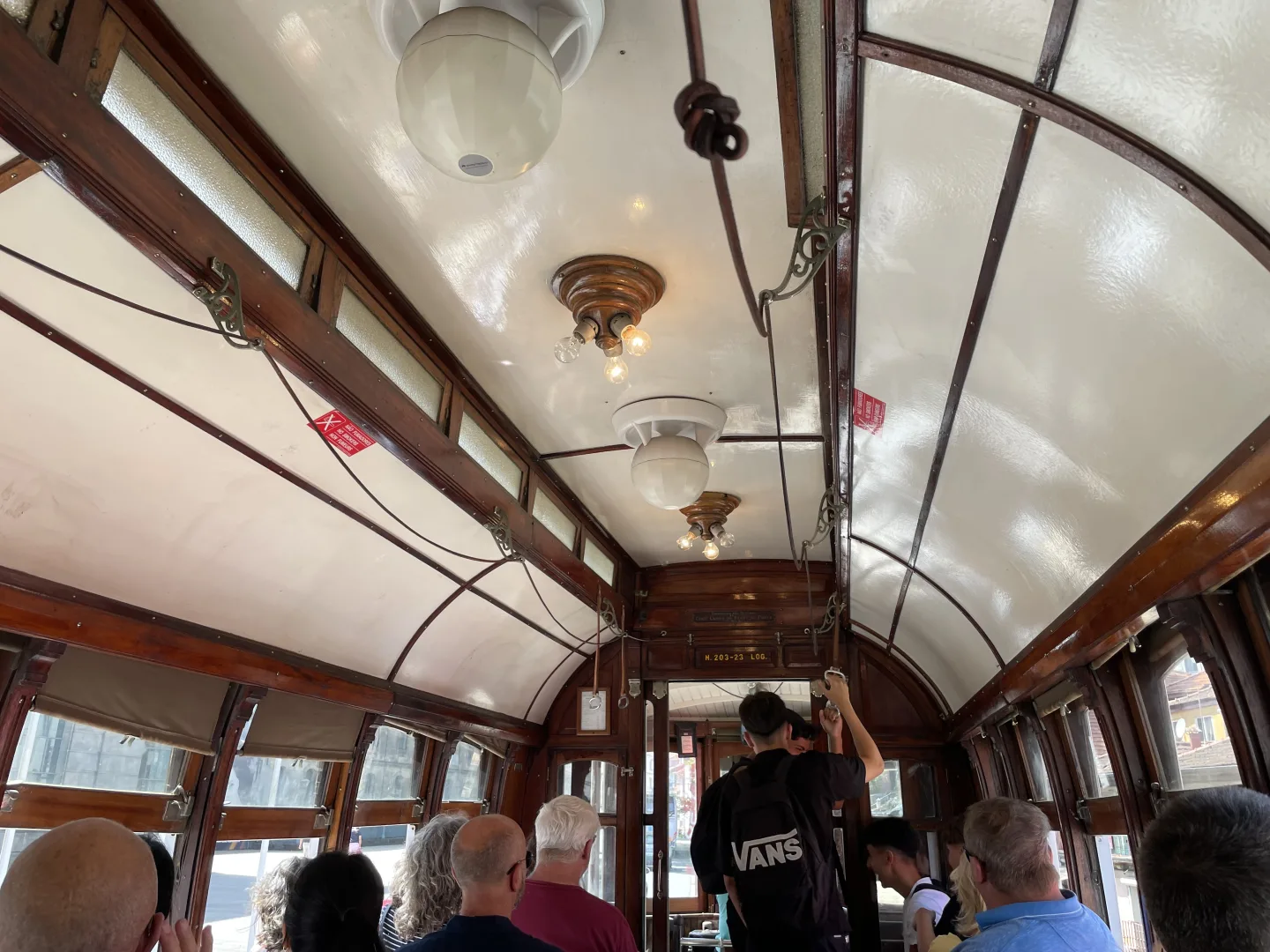 Vue intérieure d’un tramway avec ses boiseries, ses luminaires anciens et ses passagers assis